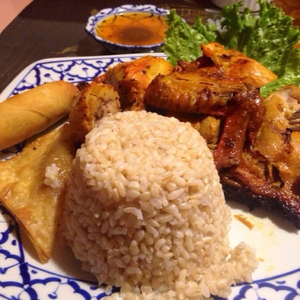 Thai grilled chicken with brown rice, egg rolls, and lettuce on a patterned plate.