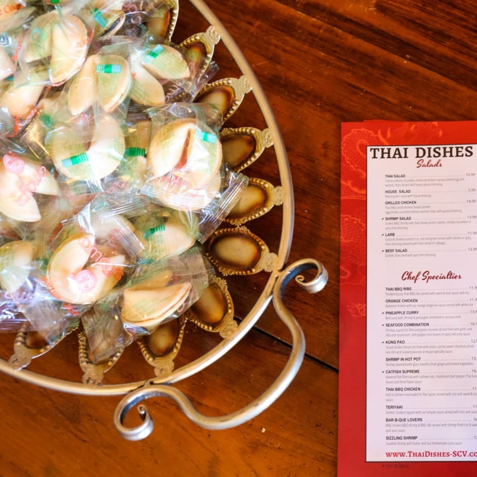 A decorative tray filled with individually wrapped fortune cookies sits beside a Thai Dishes menu.