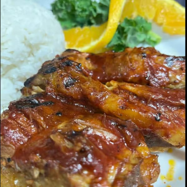 Grilled chicken with BBQ sauce, white rice, and orange slices on a white plate.