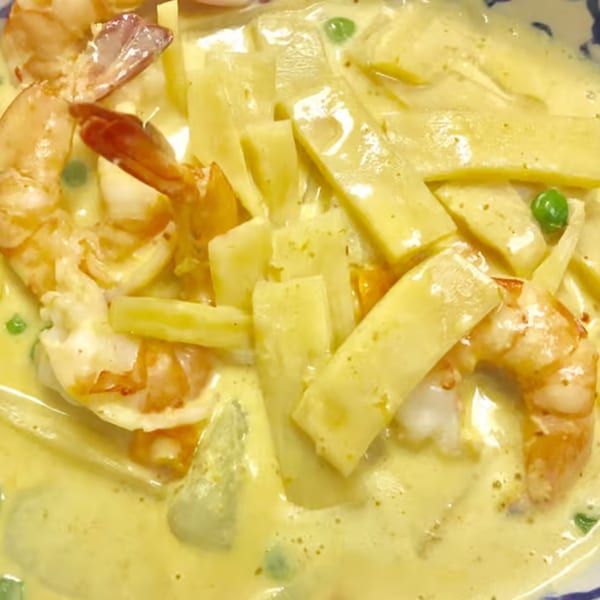 Close-up of yellow curry with shrimp, bamboo shoots, and green peas in a white bowl.
