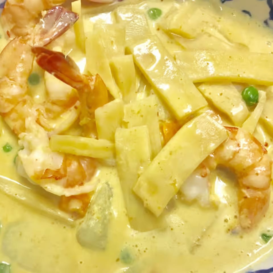 Close-up of yellow curry with shrimp, bamboo shoots, and green peas in a white bowl.