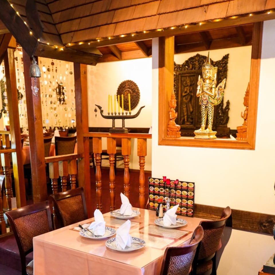 A dining table set for four with Thai decor, including a golden statue and wooden accents.
