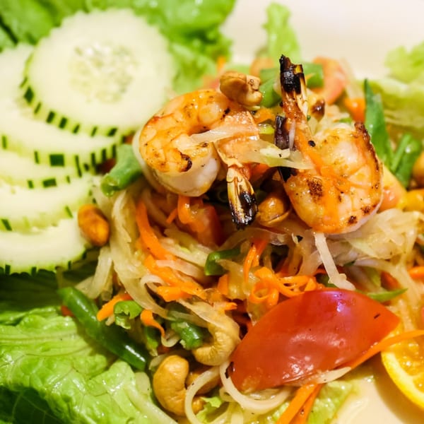 Close-up of a Thai salad with grilled shrimp, shredded papaya, cashews, and cucumber slices.