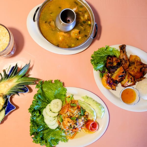 Overhead view of Thai dishes: hot pot soup, grilled chicken, shrimp salad, and pineapple.