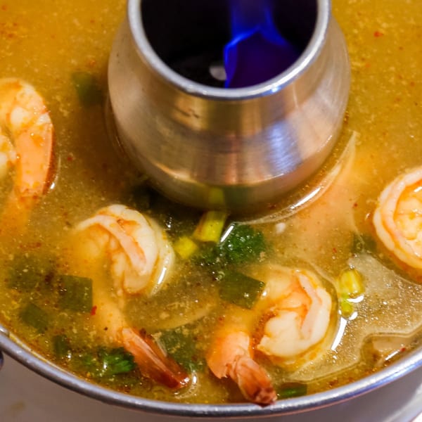 Close-up of a Thai tom yum soup with shrimp and vegetables, simmering in a hot pot with a blue flame.