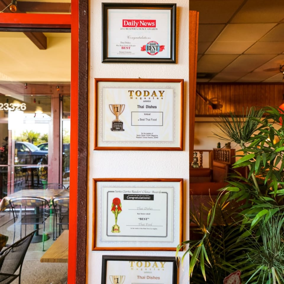 Multiple framed awards for "Best Thai Food" from various publications displayed on a wall.
