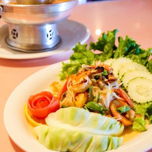 Thai papaya salad with grilled shrimp, fresh vegetables, and a decorative tomato rose.
