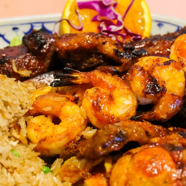 Grilled shrimp and chicken with fried rice, garnished with orange slice and red cabbage.